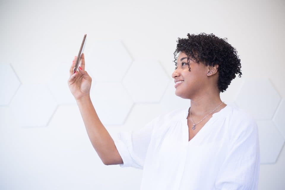 A woman in a white shirt smiling at the phone she is holding up